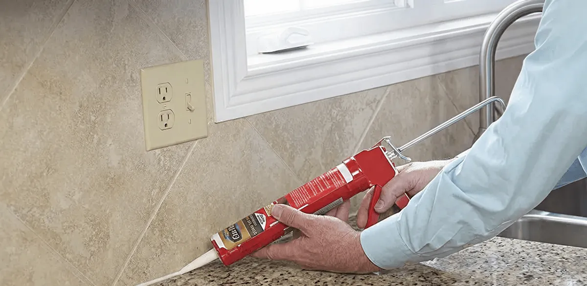 Handyman applying caulk along a kitchen backsplash and countertop seam in Buffalo, NY